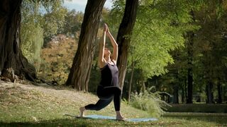 Wide View of Woman Sitting on Yoga Mat and Practicing Yoga Stretching Exercise Outdoors in Sunny Day